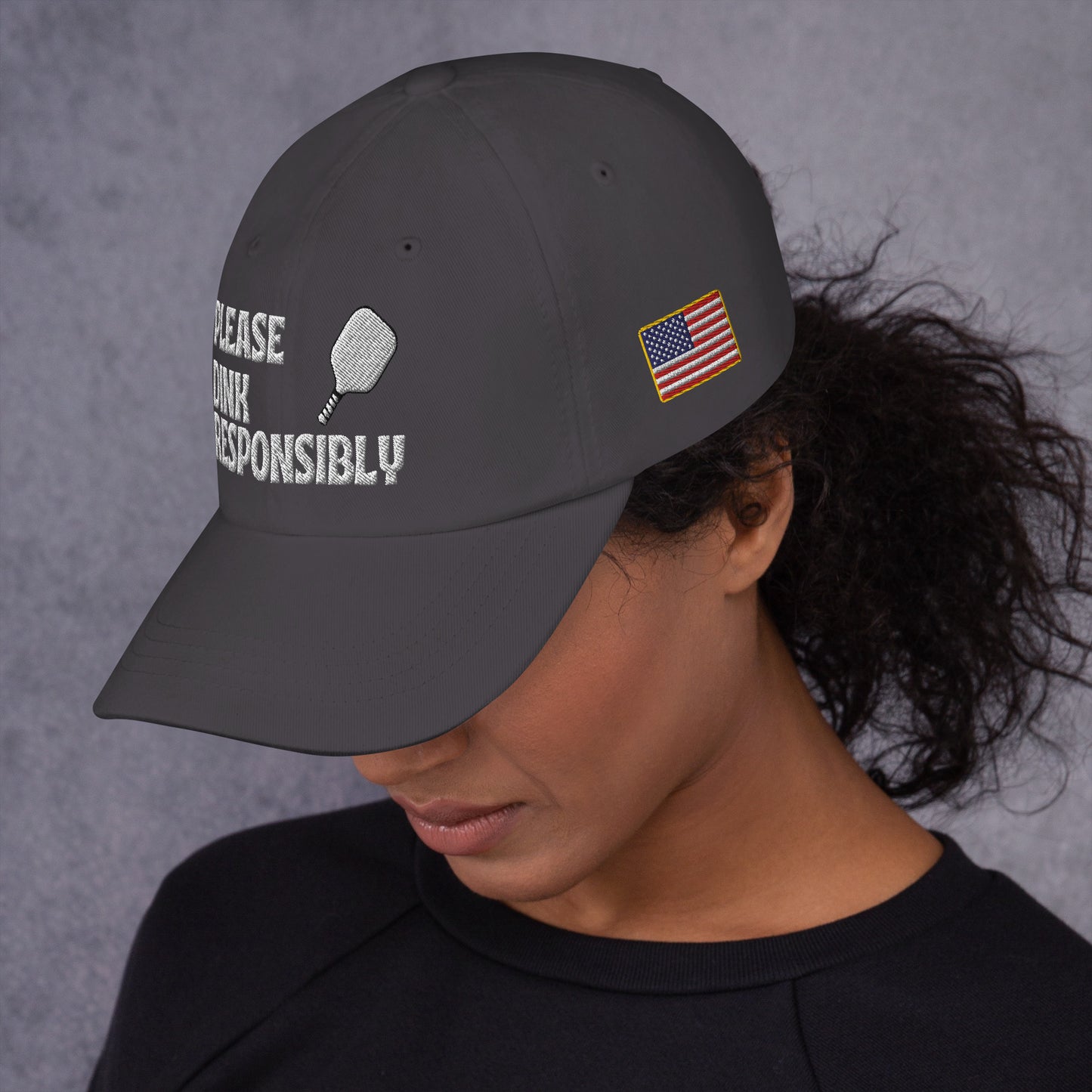 Side view of dark grey dad hat on model with "PLEASE DINK" embroidery, pickleball paddle icon, and US flag patch