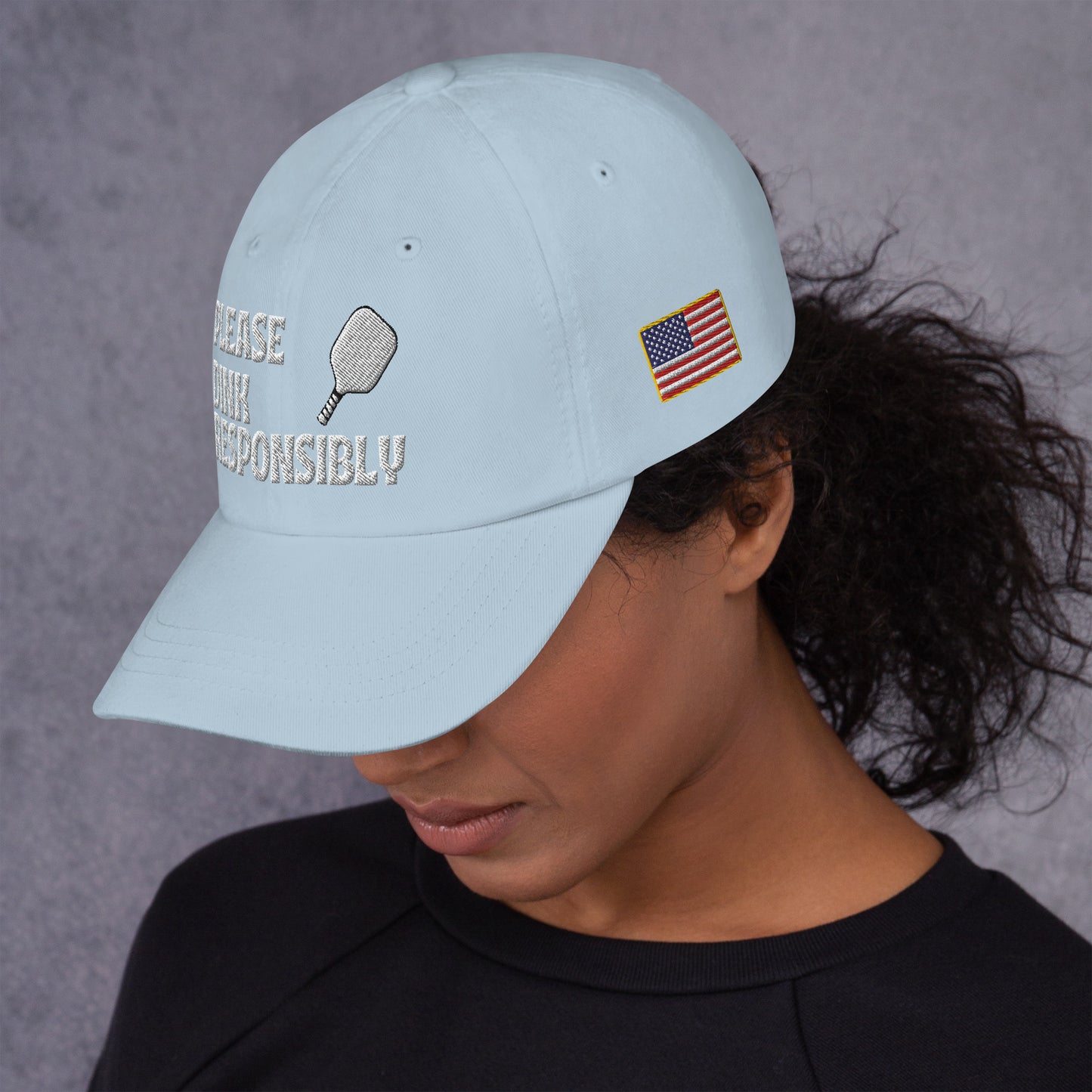 Profile view of light blue dad hat on model, visible pickleball paddle, "PLEASE DINK RESPONSIBLY" and US flag patch