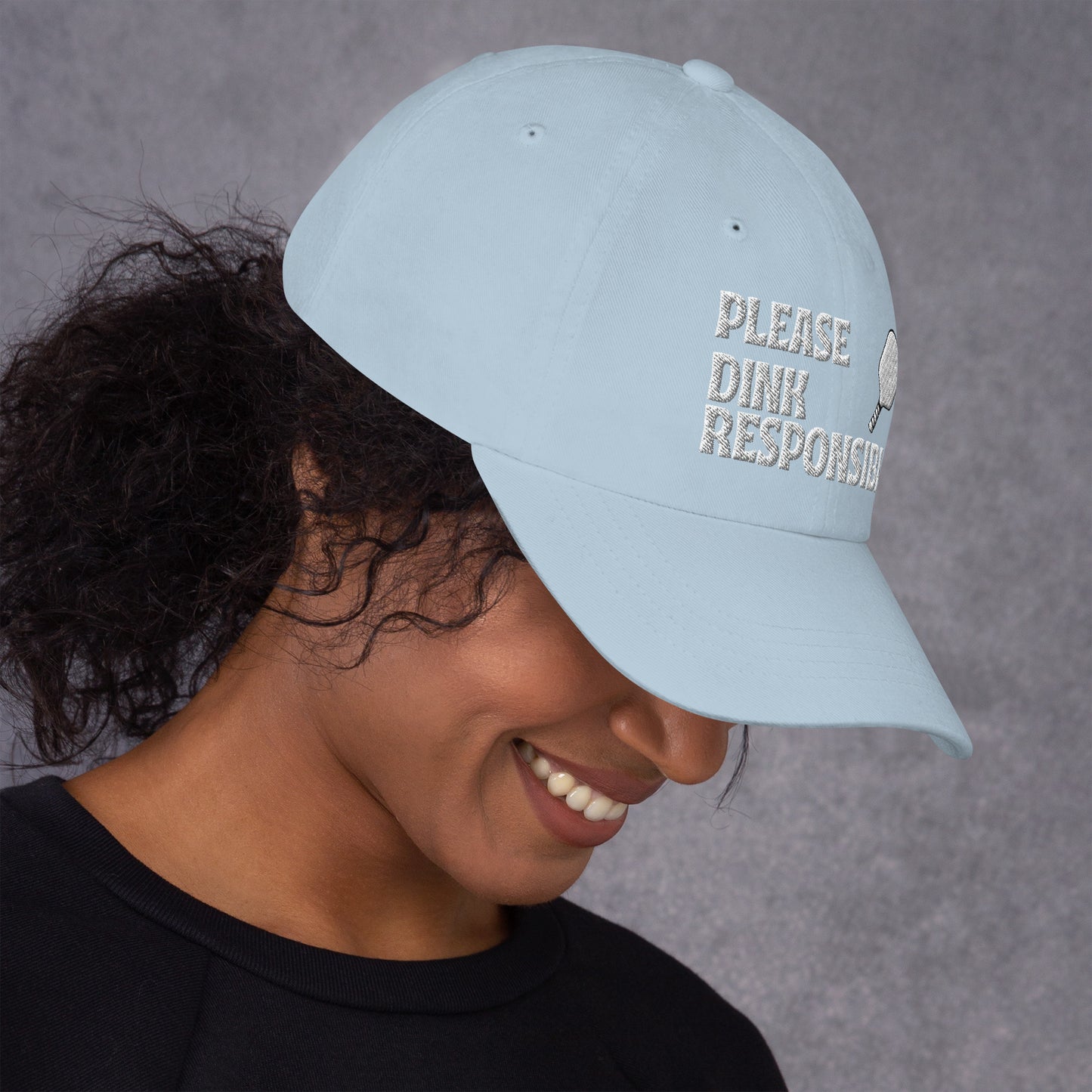 White dad hat on smiling model, "PLEASE DINK RESPONSIBLY" embroidery featuring pickleball paddle
