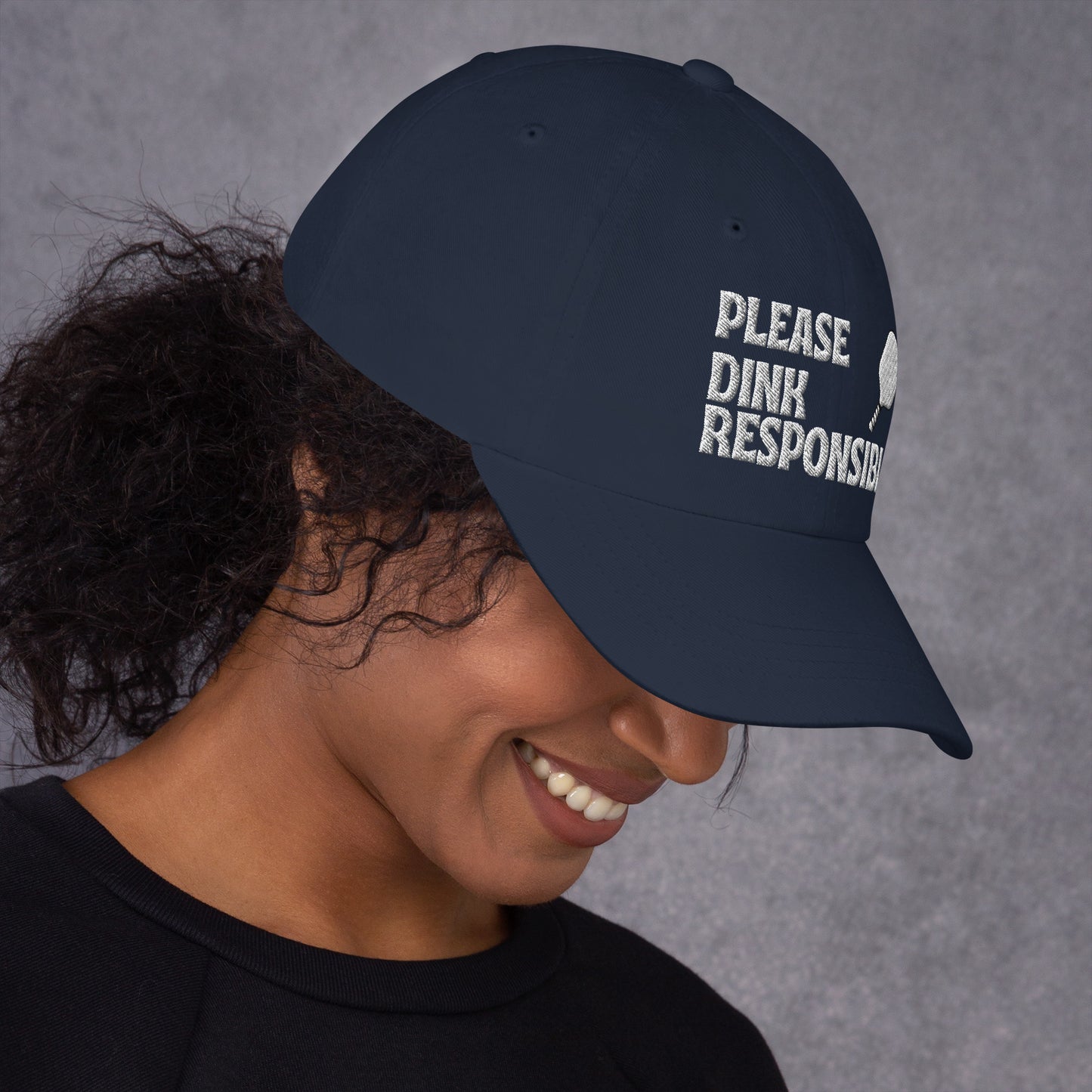 Right 3/4 view of navy dad hat on smiling model, "PLEASE DINK RESPONSIBLY" embroidery and pickleball paddle angled