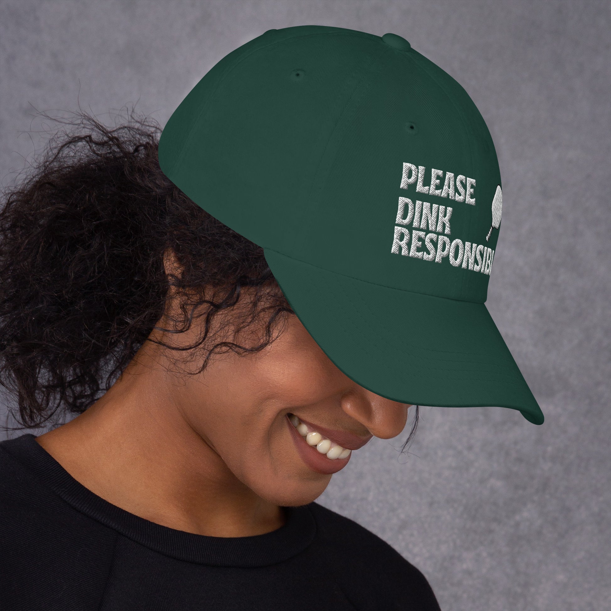 Right 3/4 view of spruce green dad hat on smiling model, "PLEASE DINK RESPONSIBLY" embroidery and pickleball paddle angled