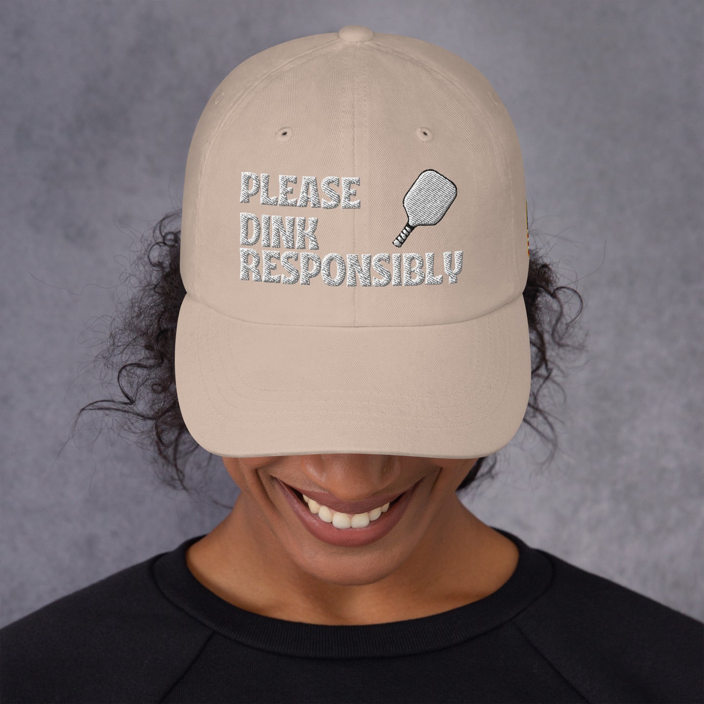 Frontish view under khaki dad hat on grinning model with "PLEASE DINK RESPONSIBLY" and pickleball