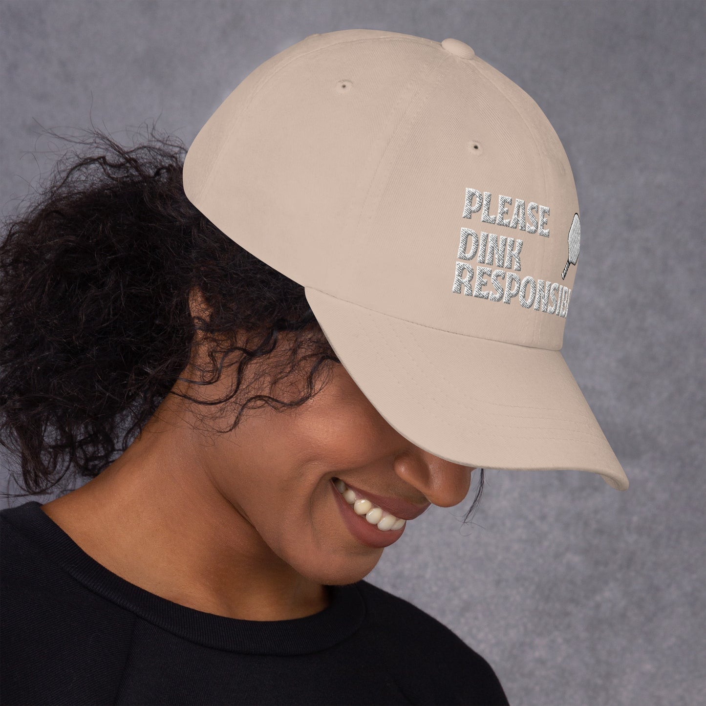 Model under pink dad hat smiling with "PLEASE DINK RESPONSIBLY" embroidery and pickleball paddle