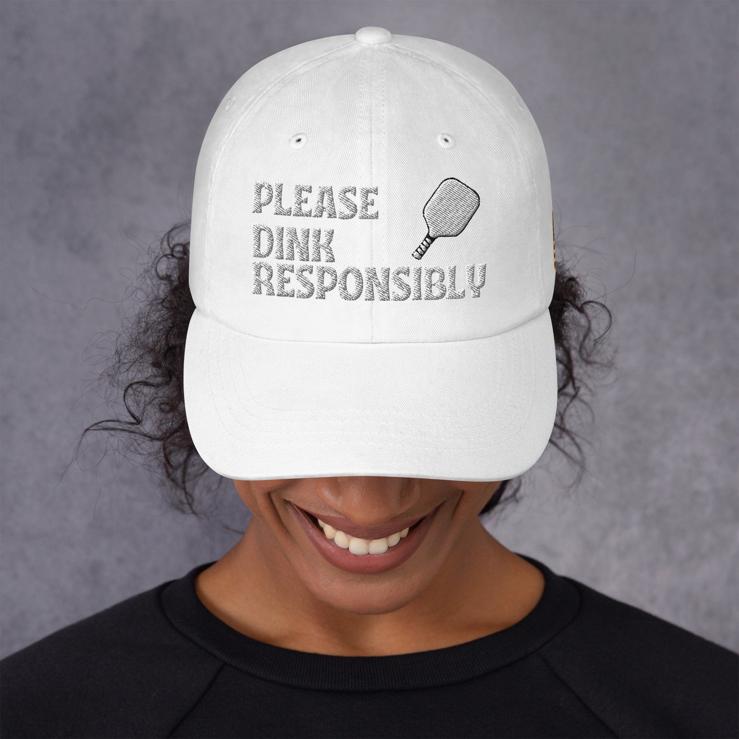 Angled white dad hat on model, "PLEASE DINK RESPONSIBLY" text, pickleball paddle and US flag patch