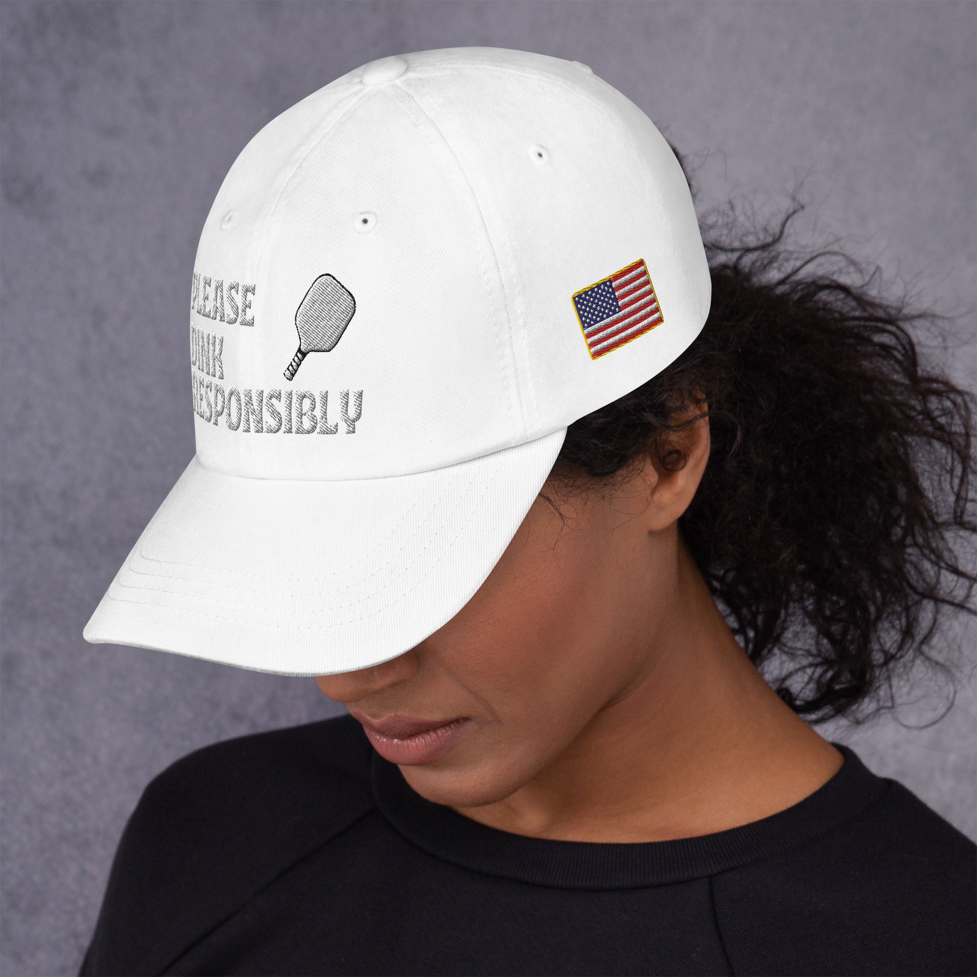 Close-up smiling model wearing white dad hat with "PLEASE DINK RESPONSIBLY" and pickleball paddle embroidery