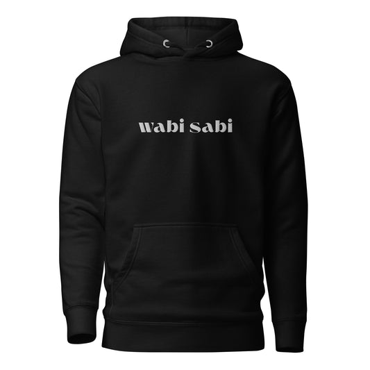 Front view of black unisex hoodie with light "wabi sabi" embroidery, pouch pocket, cozy pullover vibes