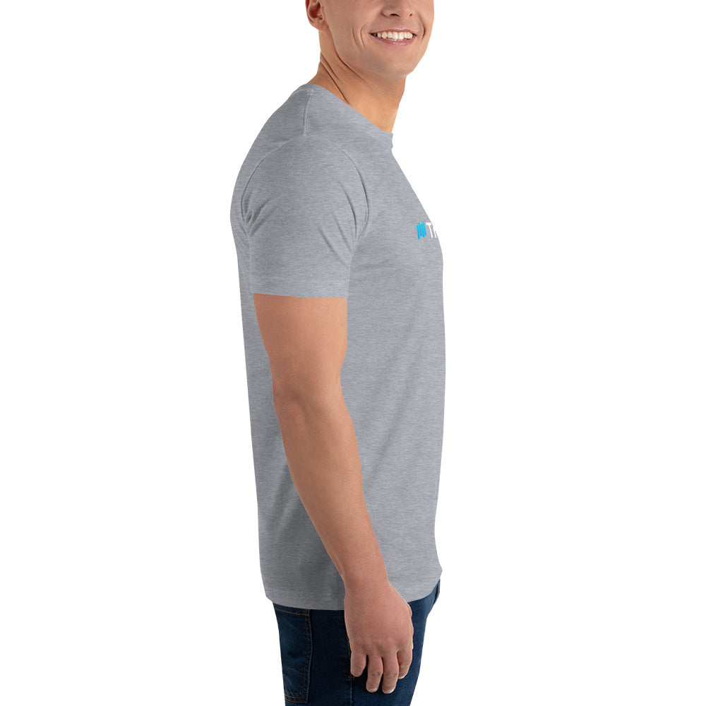 Left-side view of model in heather grey fitted tee with partial teal-and-white "#TradeCaster" on chest