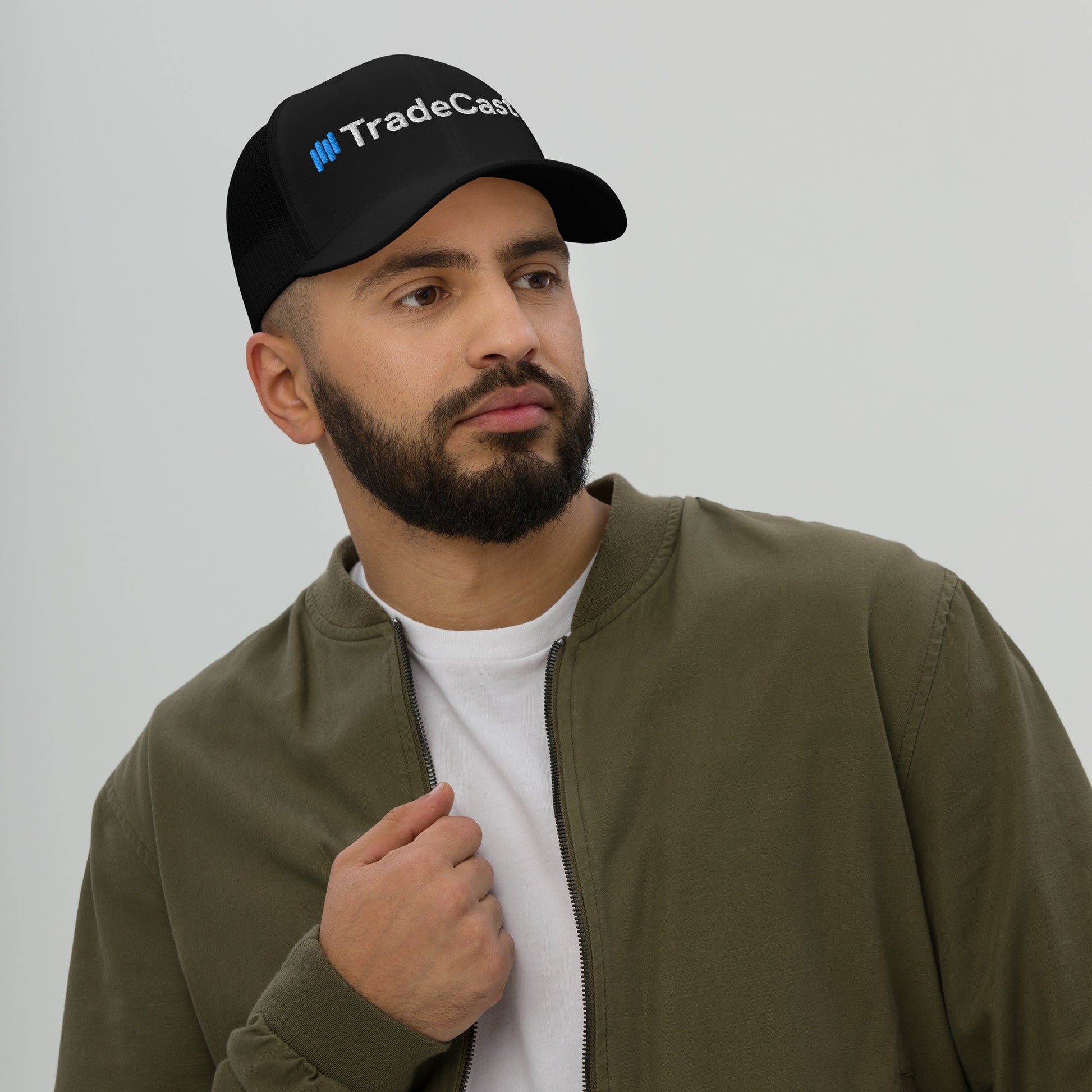 Side profile of bearded guy in black TradeCaster trucker cap, mesh back breezy, blue embroidery sharp