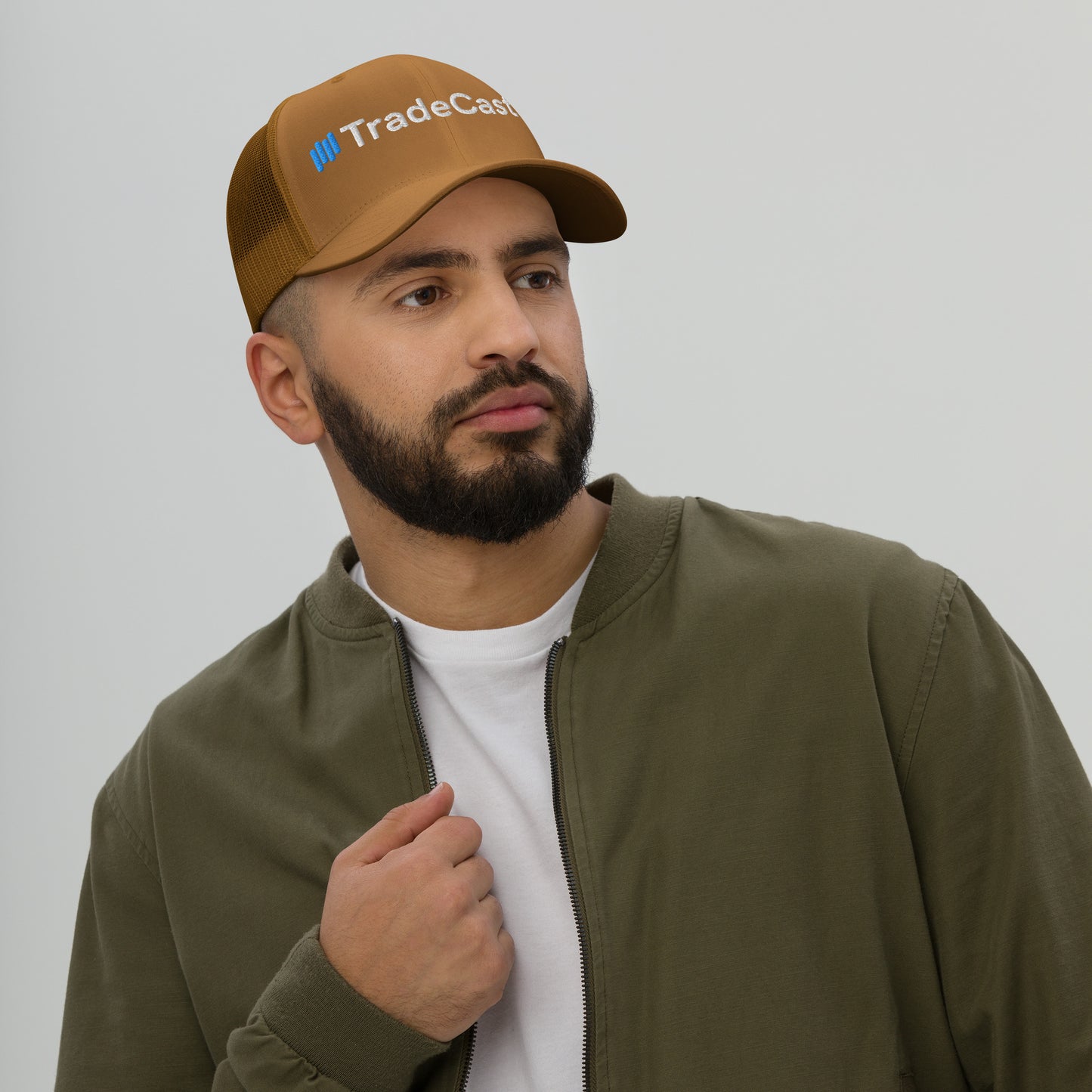 Woman in evergreen TradeCaster trucker cap, arms crossed smirking in gray patterned jacket