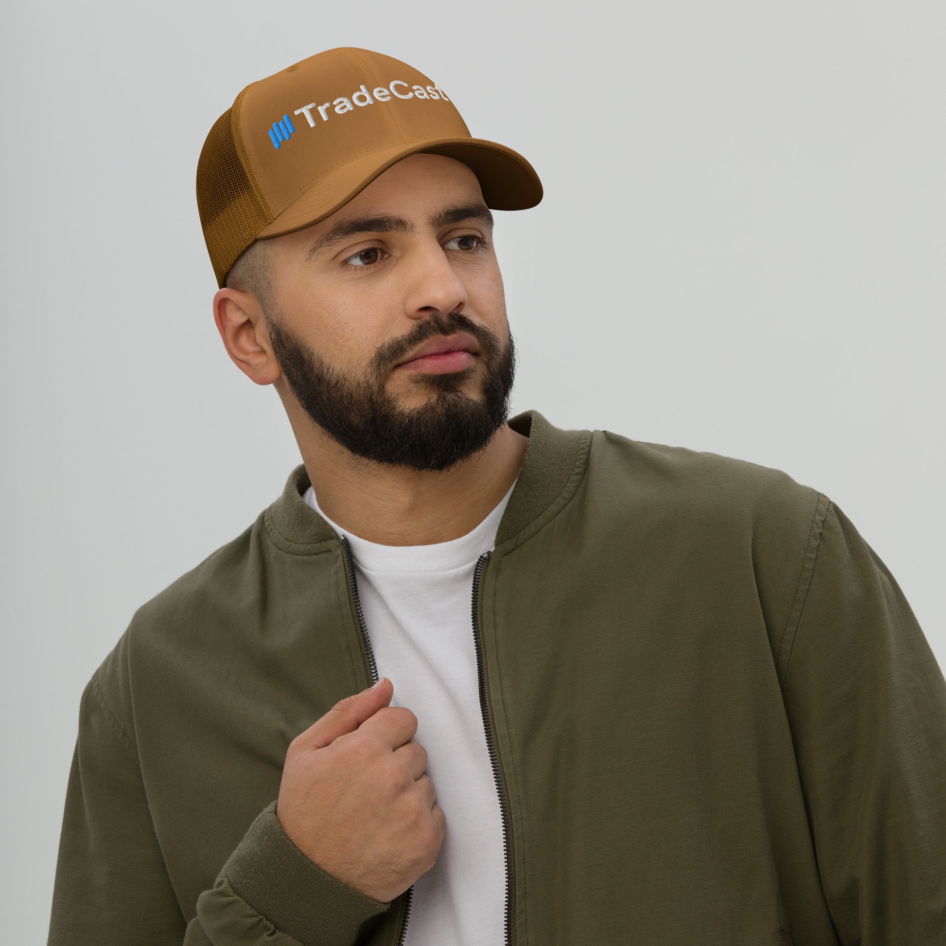 Woman in evergreen TradeCaster trucker cap, arms crossed smirking in gray patterned jacket