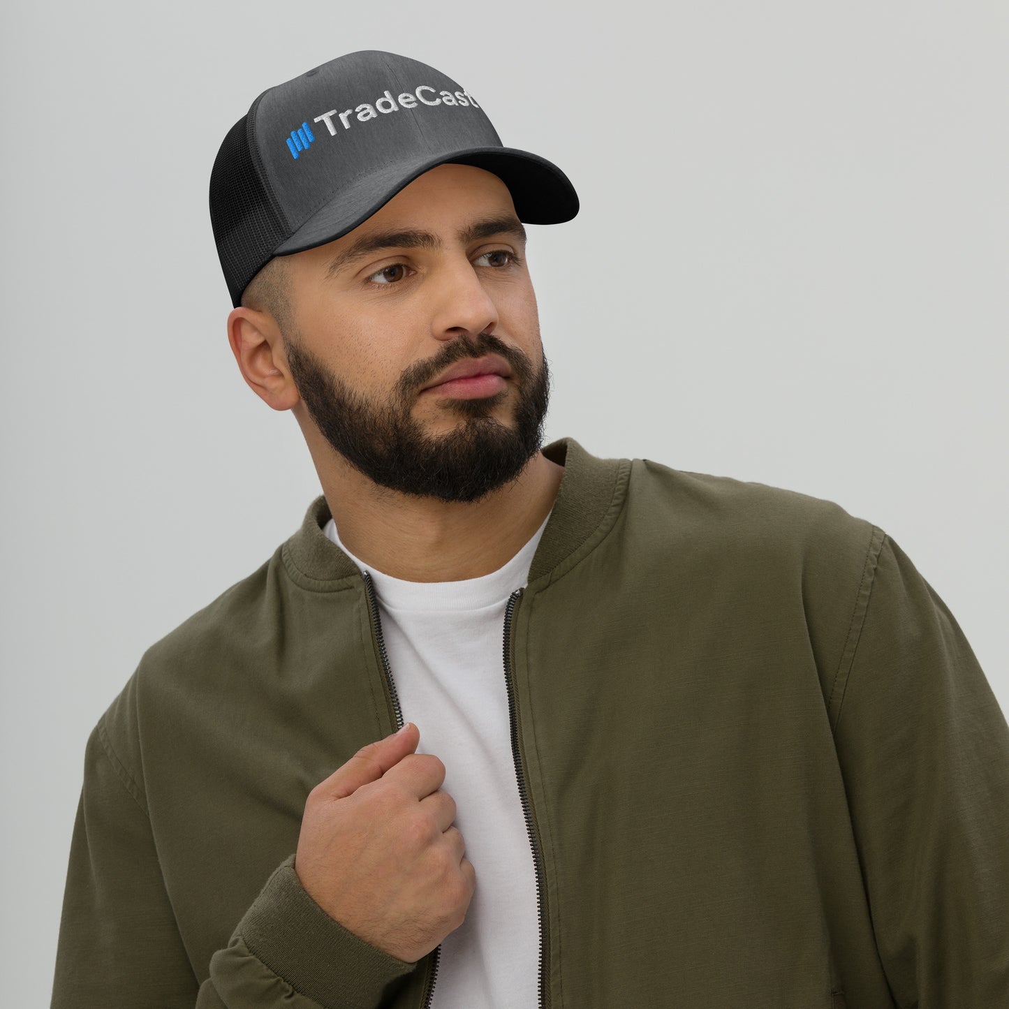 Bearded guy side view pondering in black TradeCaster cap, white shirt olive bomber jacket