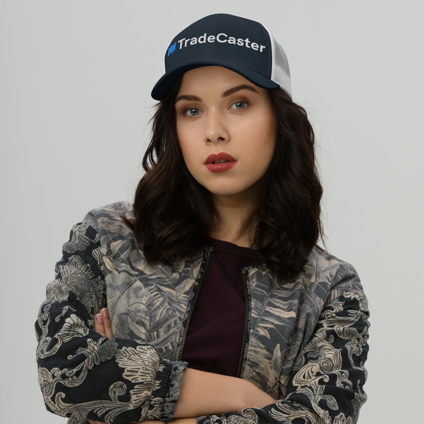 Navy TradeCaster trucker cap front on model with arms crossed, white mesh back, gray jacket slay