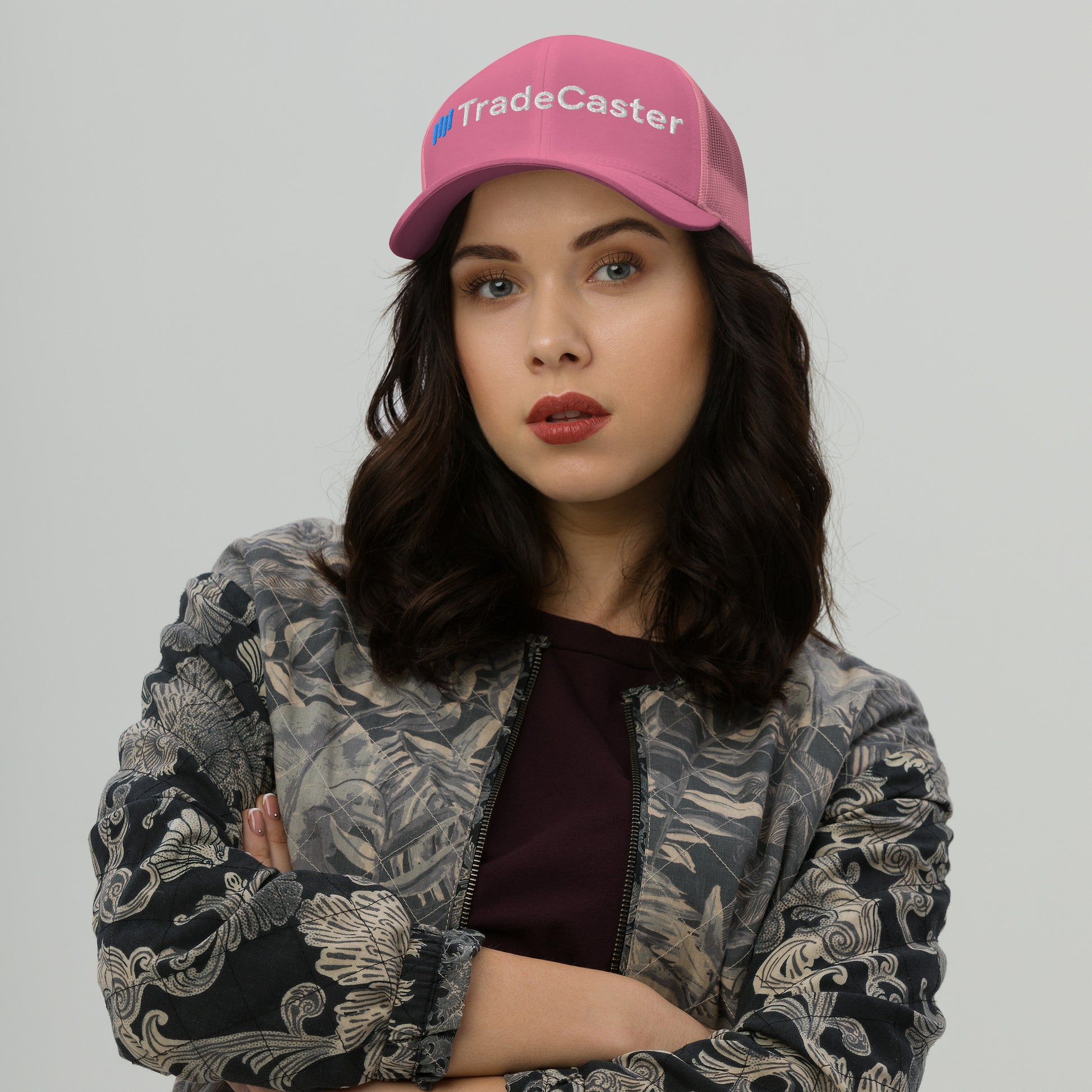 Front view model owning hot pink TradeCaster trucker cap, arms crossed, pouting in patterned gray jacket