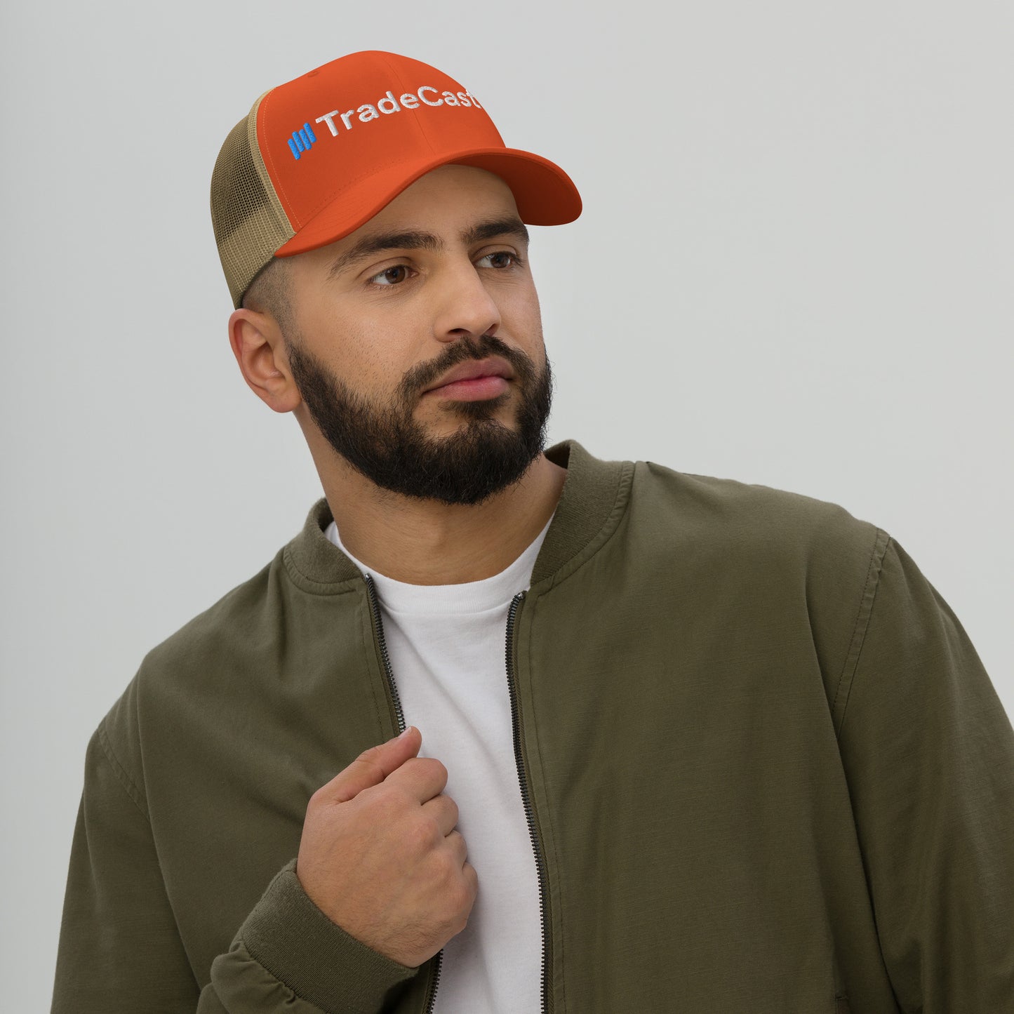 Guy's side profile in orange camo-mesh TradeCaster trucker, white tee, green jacket casual