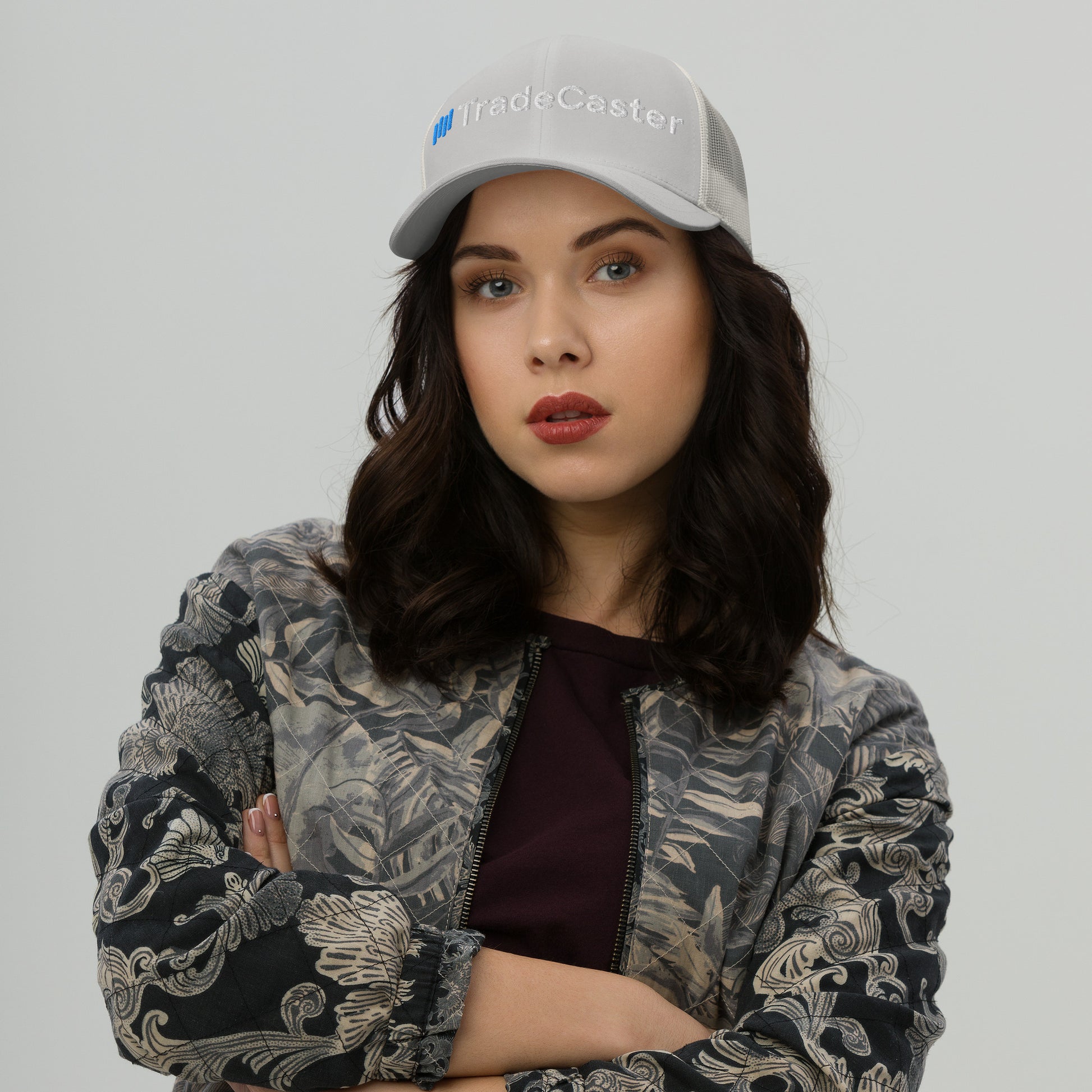 Model owning dark heather gray TradeCaster cap, stern pose arms crossed in embroidered gray jacket