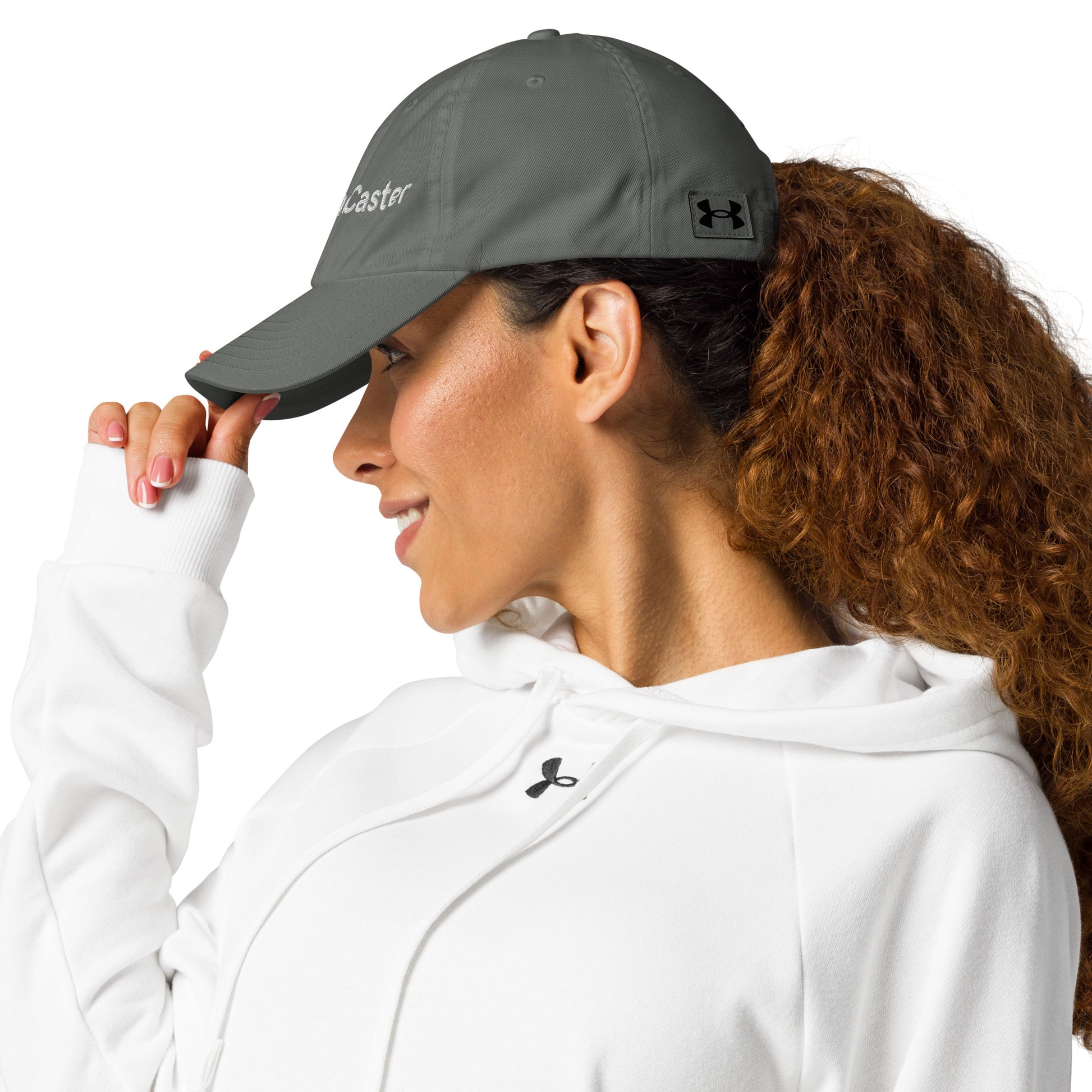 Woman modeling left side of gray Under Armour TradeCaster hat, white embroidery sharp, UA logo detail, effortless pose
