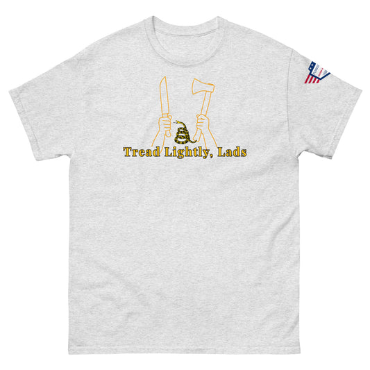 Front view of light gray unisex tee with gold "Tread Lightly, Lads" print, hands gripping knife & axe around coiled Gadsden snake, US flag sleeve patch