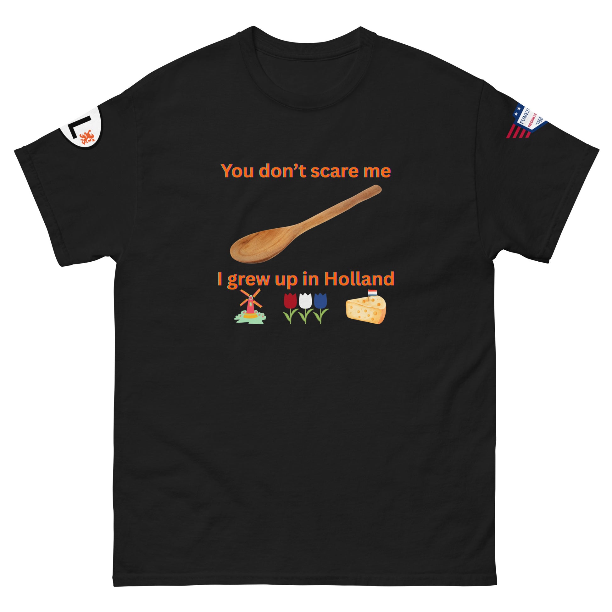 Front view of black unisex tee with orange "You don't scare me, I grew up in Holland" print, wooden spoon, windmill/tulip/cheese emojis, sleeve patches