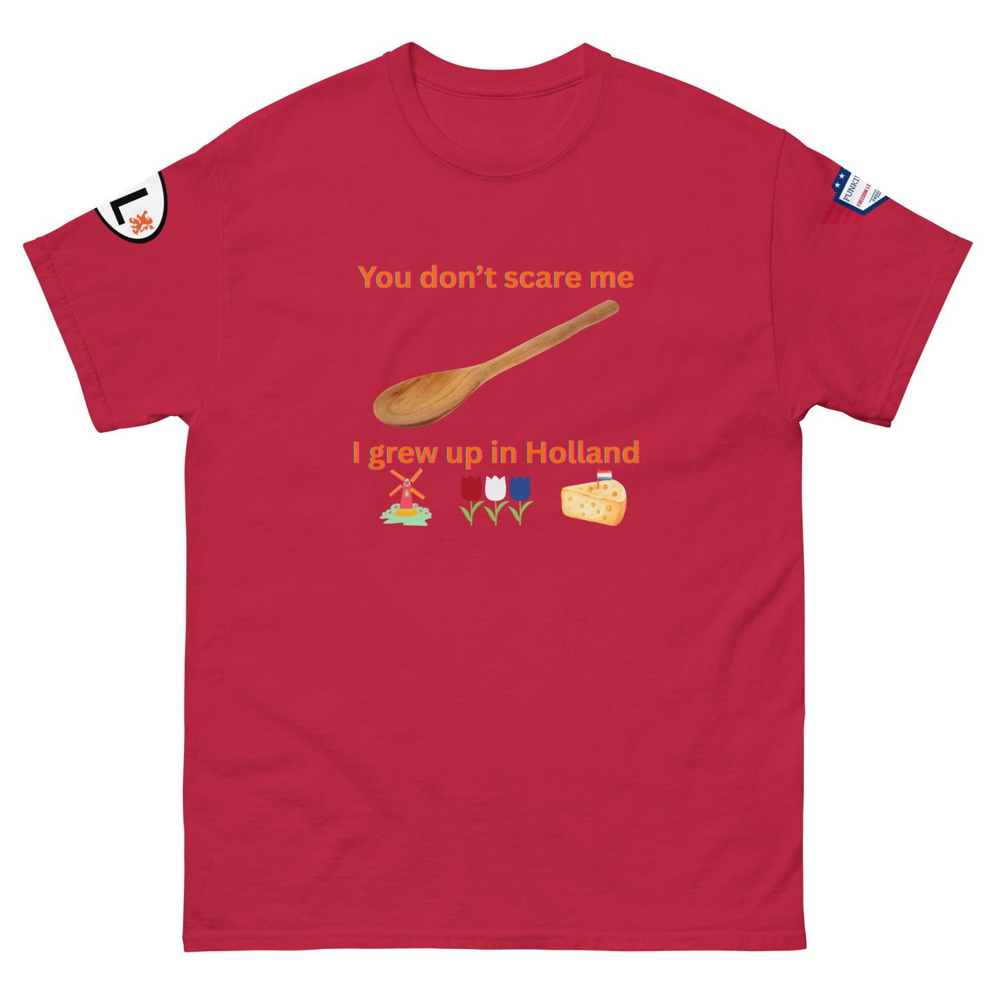 Front view of red unisex tee with orange "You don't scare me, I grew up in Holland" print, wooden spoon, windmill/tulip/cheese emojis, sleeve patches