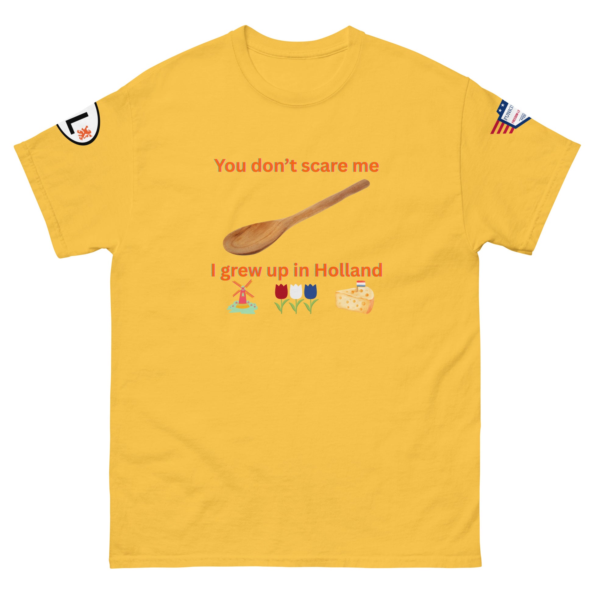 Front view of mustard yellow unisex tee with orange "You don't scare me, I grew up in Holland" print, wooden spoon, windmill/tulip/cheese emojis, sleeve patches