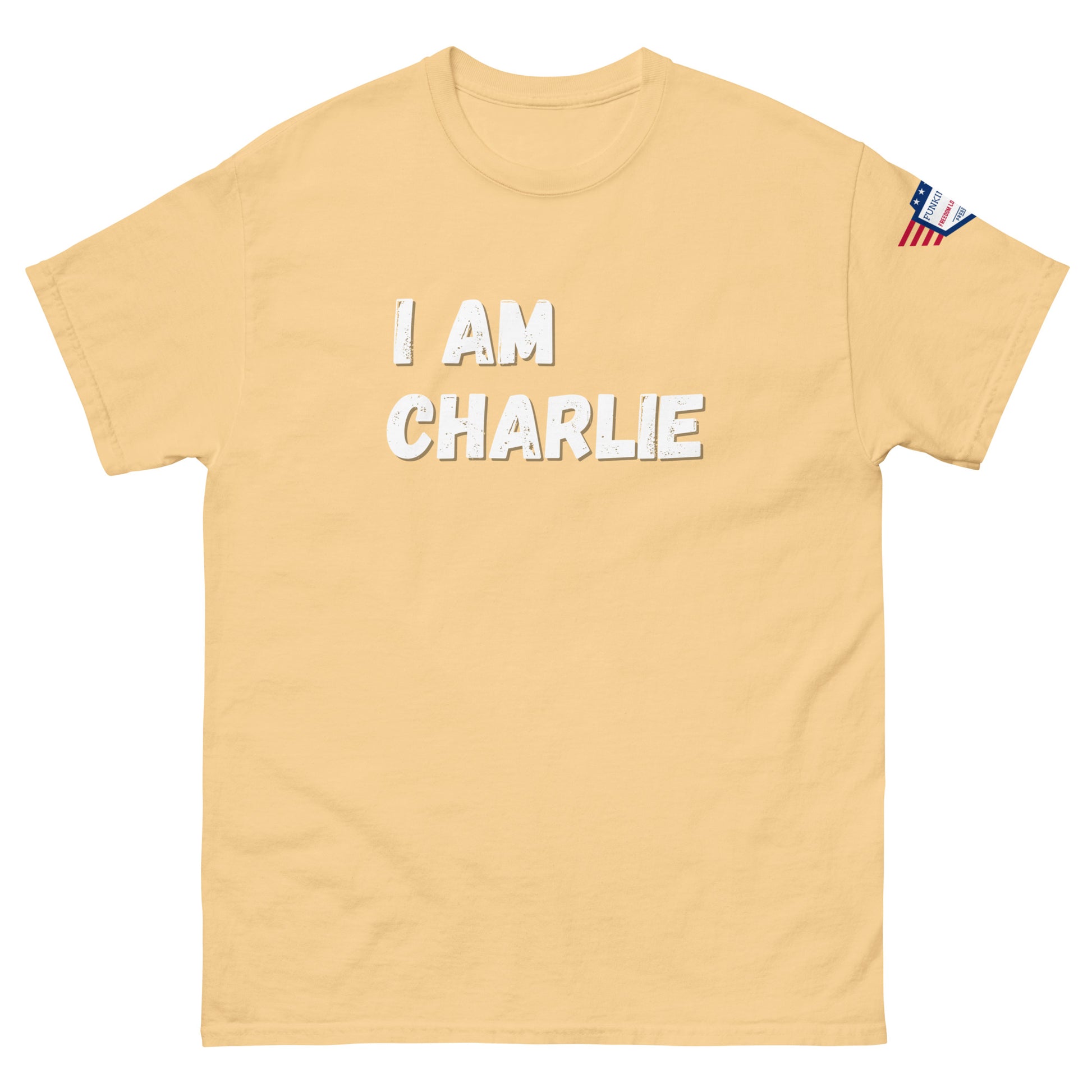 Front view of beige unisex tee with bold white "I AM CHARLIE" graphic and small USA flag sleeve patch