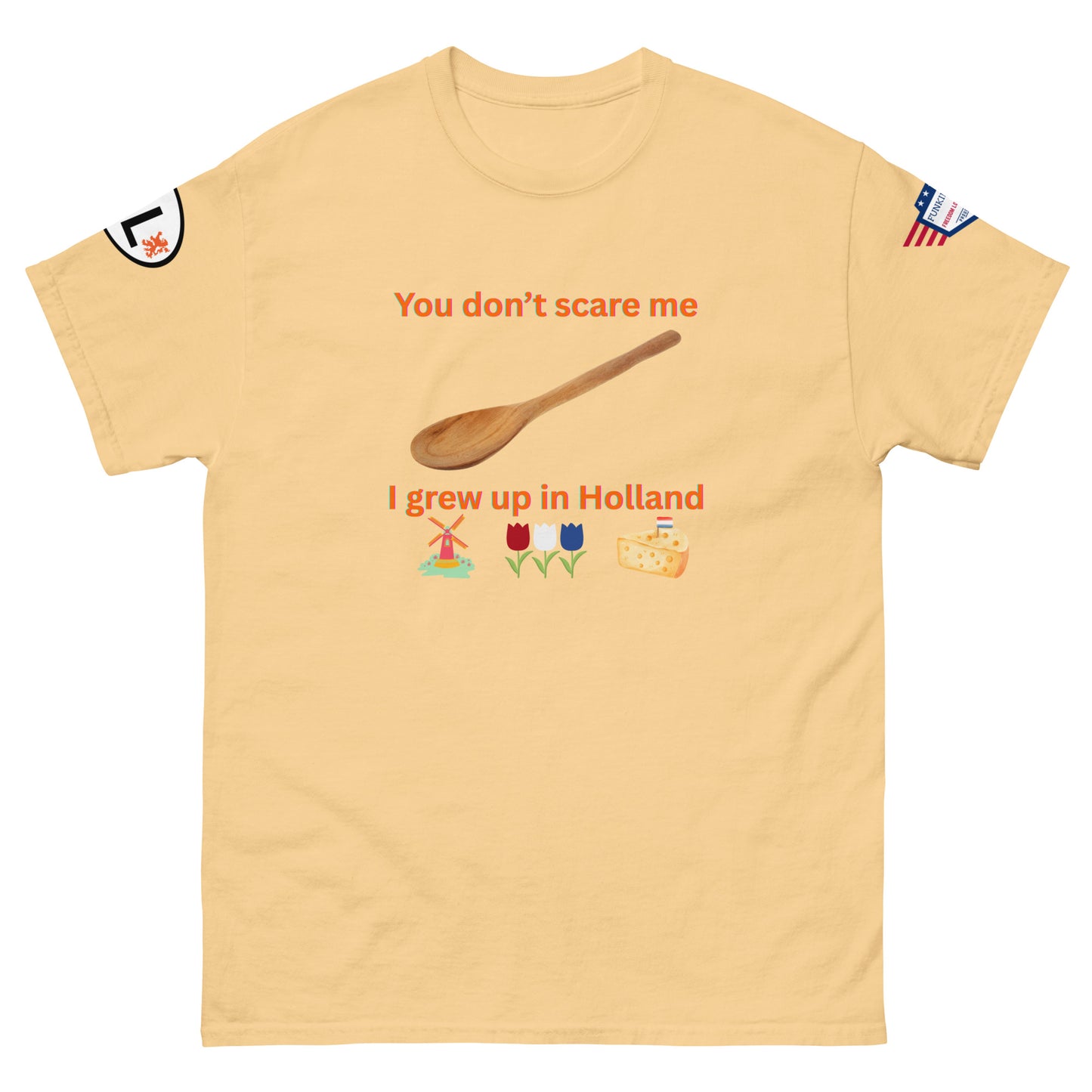 Front view of beige unisex tee with "You don't scare me I grew up in Holland" orange print, wooden spoon, windmill, tulips, cheese emojis, sleeve patches