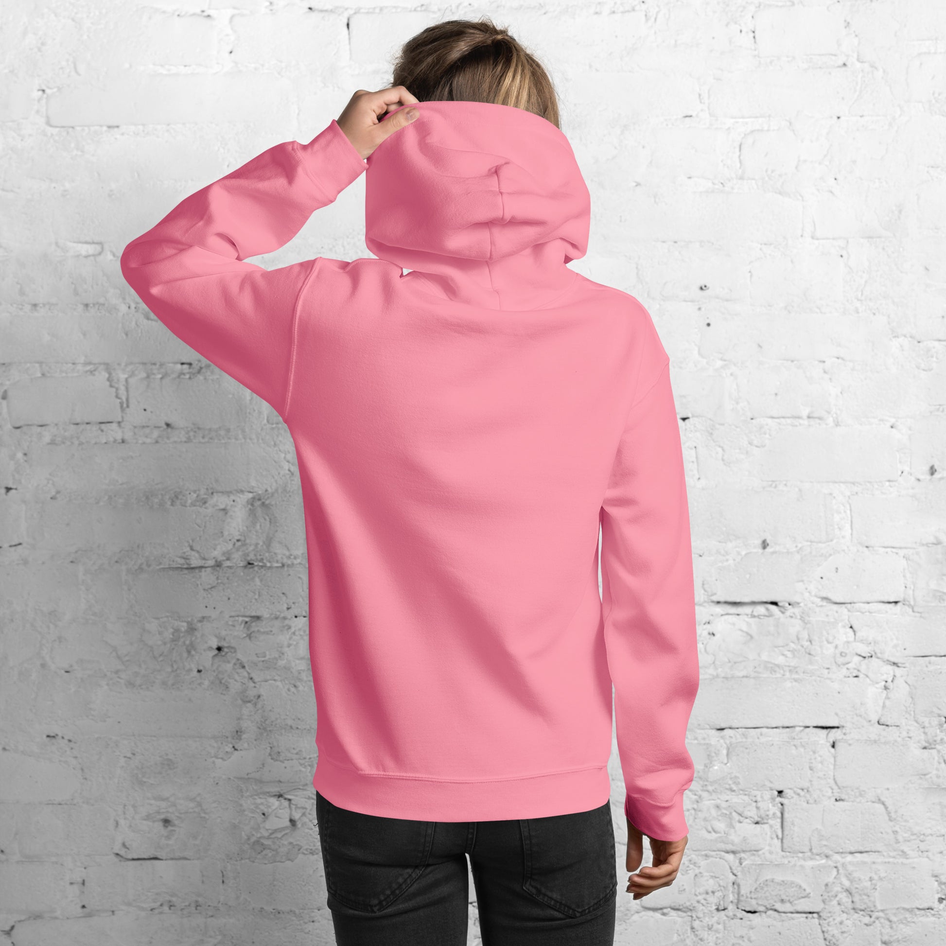 Profile right side of model in plain-back hot pink hoodie against white brick wall