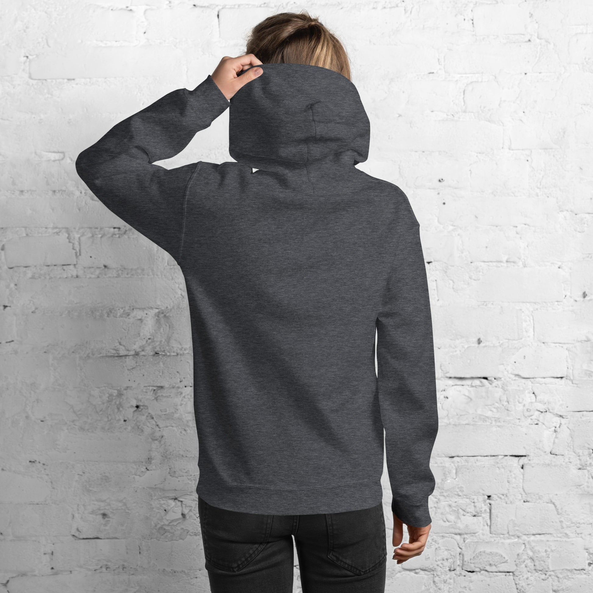 Back view of heather gray hoodie on model looking over shoulder against white brick wall