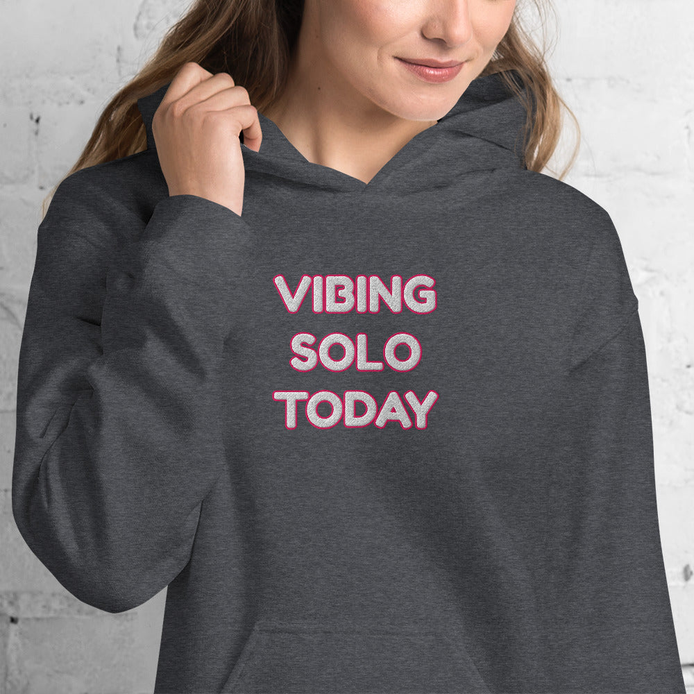 Close-up front view on smiling model wearing heather gray hoodie, pink "VIBING SOLO TODAY" embroidery