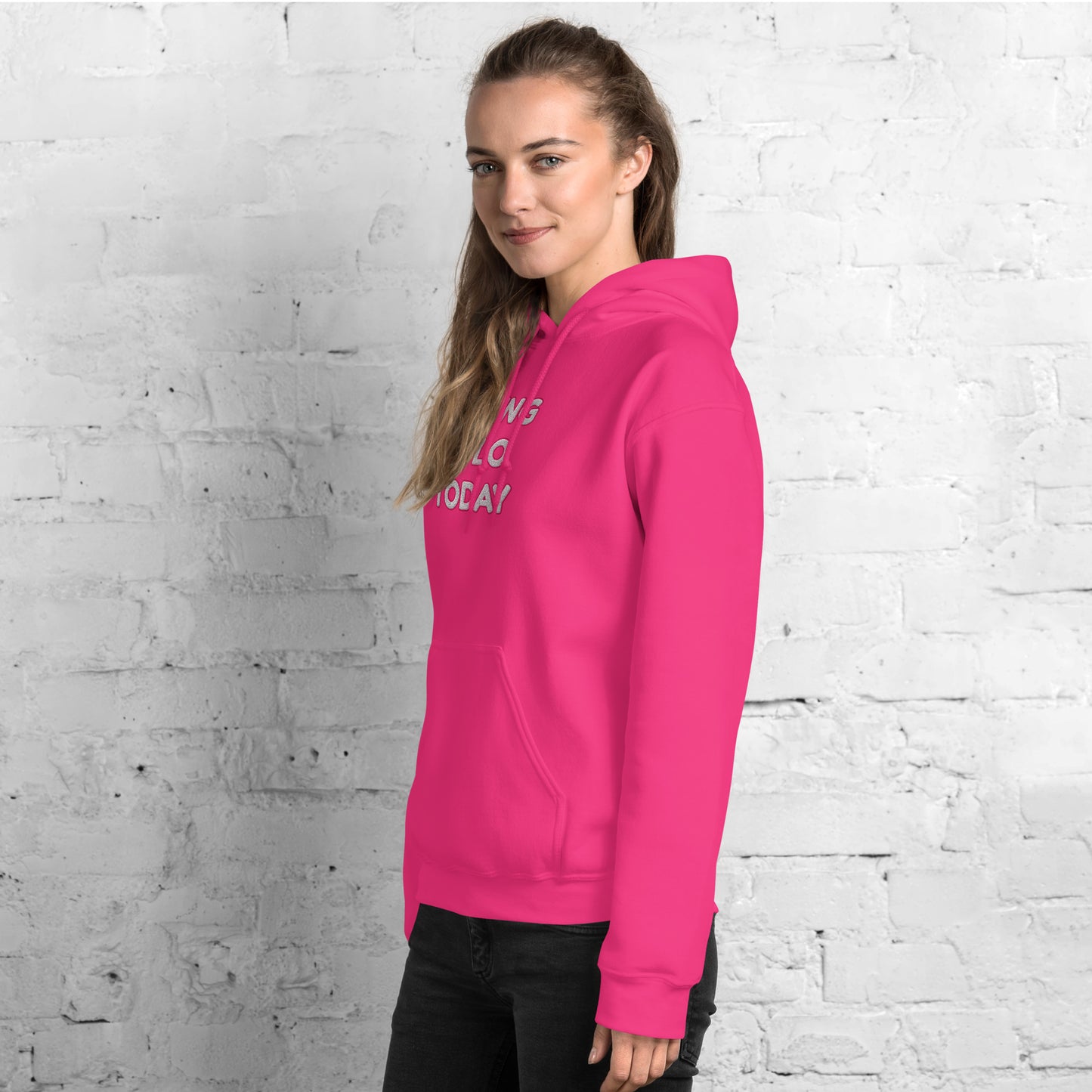 Back view of hot pink hoodie on model glancing over shoulder, white brick wall