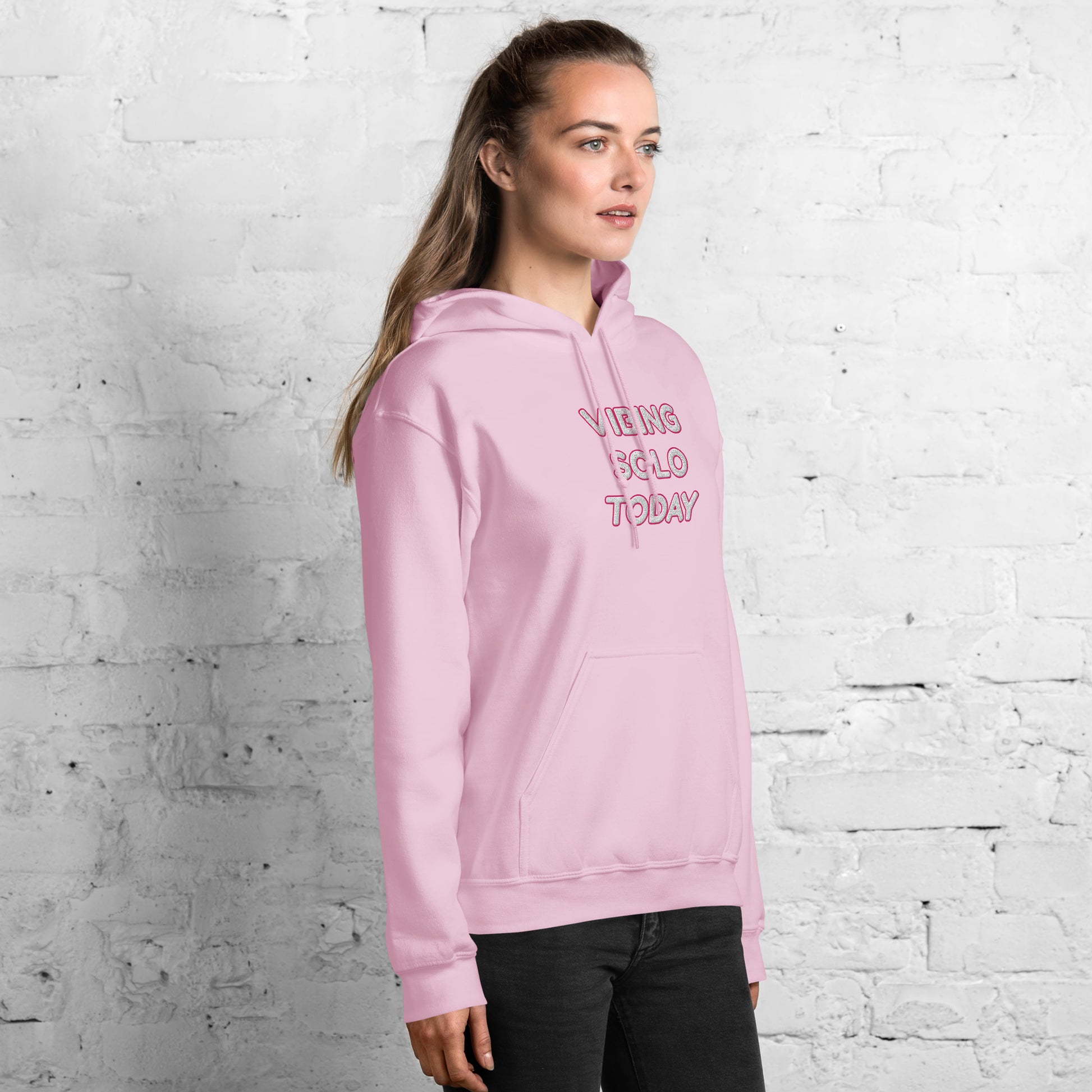 Side view of female model in light pink hoodie with "VIBING SOLO TODAY" embroidery on chest, ponytail and jeans
