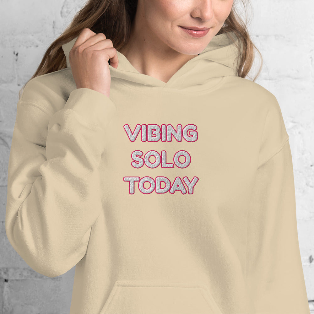 Front view of model in sand beige hoodie with pink "VIBING SOLO TODAY" embroidery, wavy hair