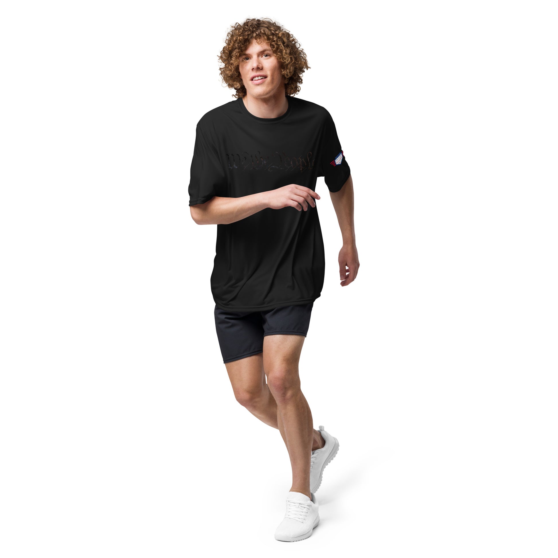 Curly-haired guy striding in black "We The People" tee, flag sleeve, athletic shorts and sneakers