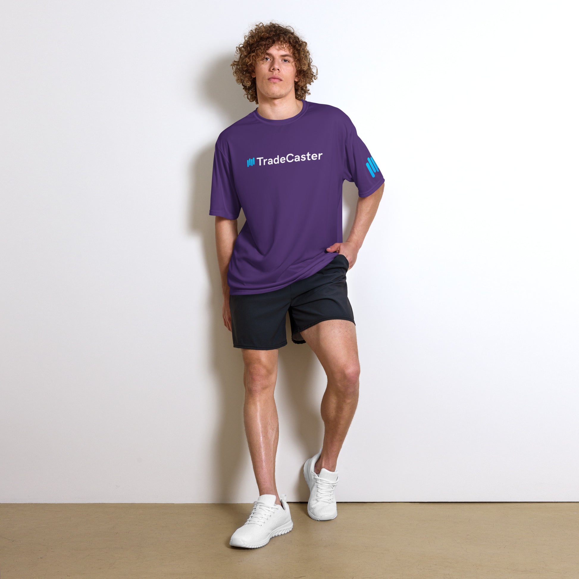 Curly-haired model flexing in front-view purple TradeCaster tee, bold cyan #TradeCaster chest print and sleeve patch